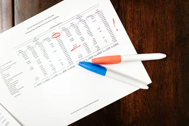 Top view of financial document with red marks and pens on wooden table surface. B2B marketing automation mistakes seen from the repair side