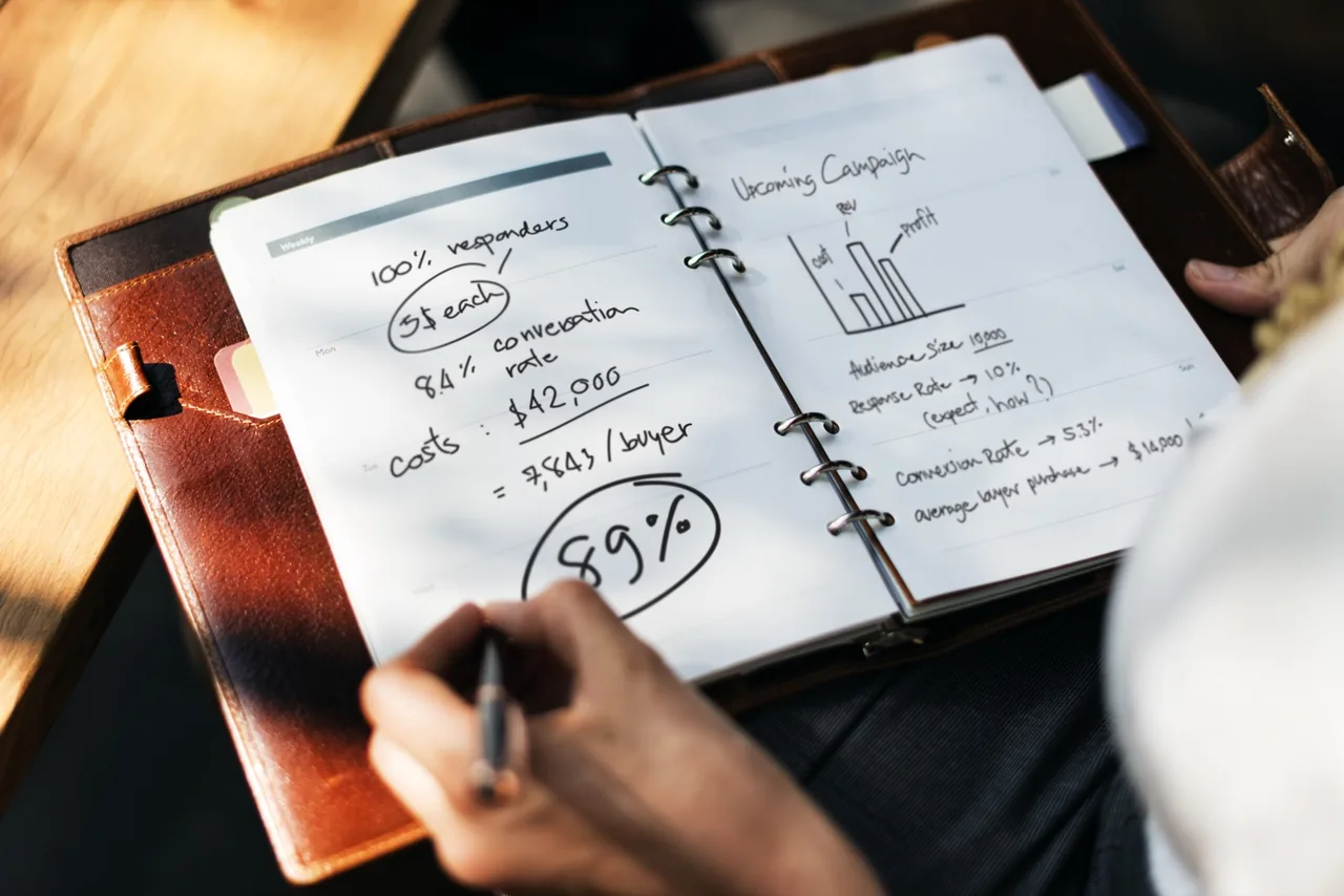 Person writing a marketing campaign plan in a notebook.